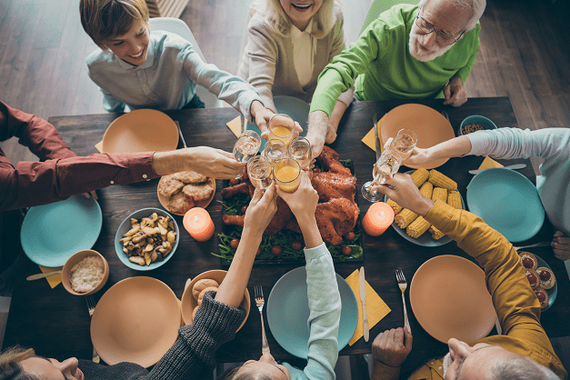Family sitting around a table eating and cheering drinks.